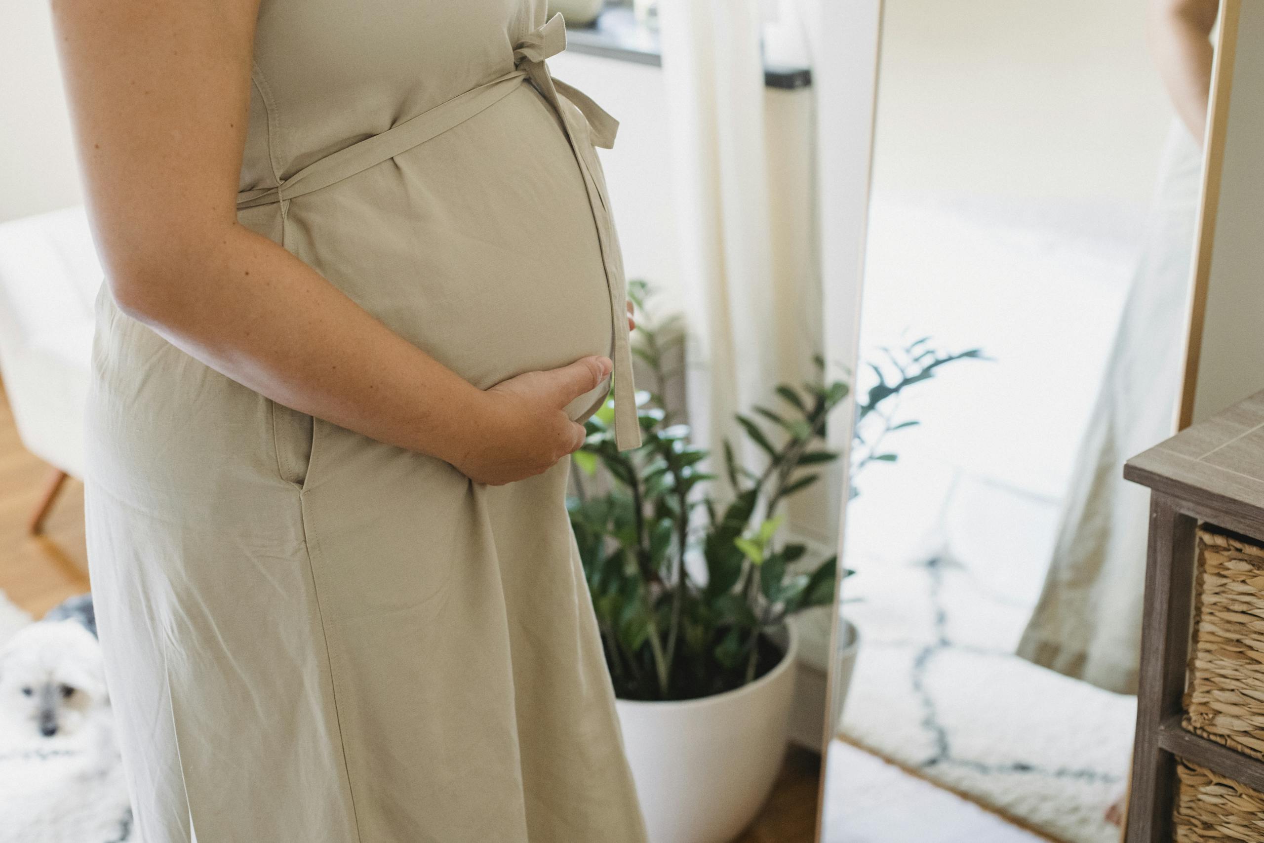 Peaceful pregnant woman at home, gently holding her belly near a mirror